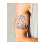 Un potente cobra con il cappuccio gonfio, attorcigliato e pronto a colpire. Questo tatuaggio simboleggia pericolo, forza e protezione, catturando la presenza intensa e dominante del re dei serpenti.
