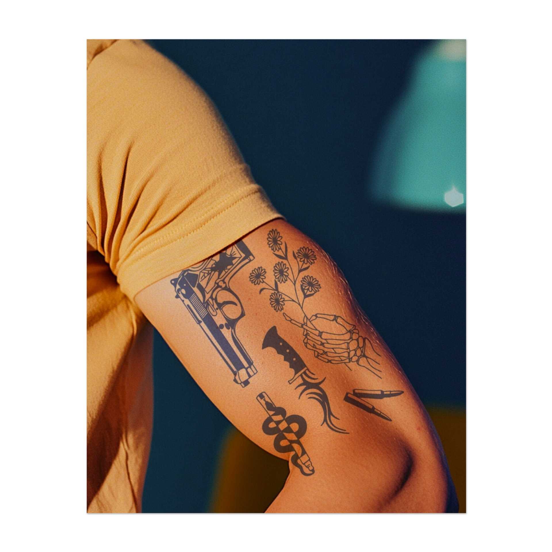 Un insieme di simboli contrastanti: una pistola, un coltello, una mano scheletrica, un serpente, un mazzo di fiori e un proiettile. Questi disegni rappresentano l'equilibrio tra vita e morte, pericolo e bellezza, e catturano sia l'eleganza che la potenza pura.