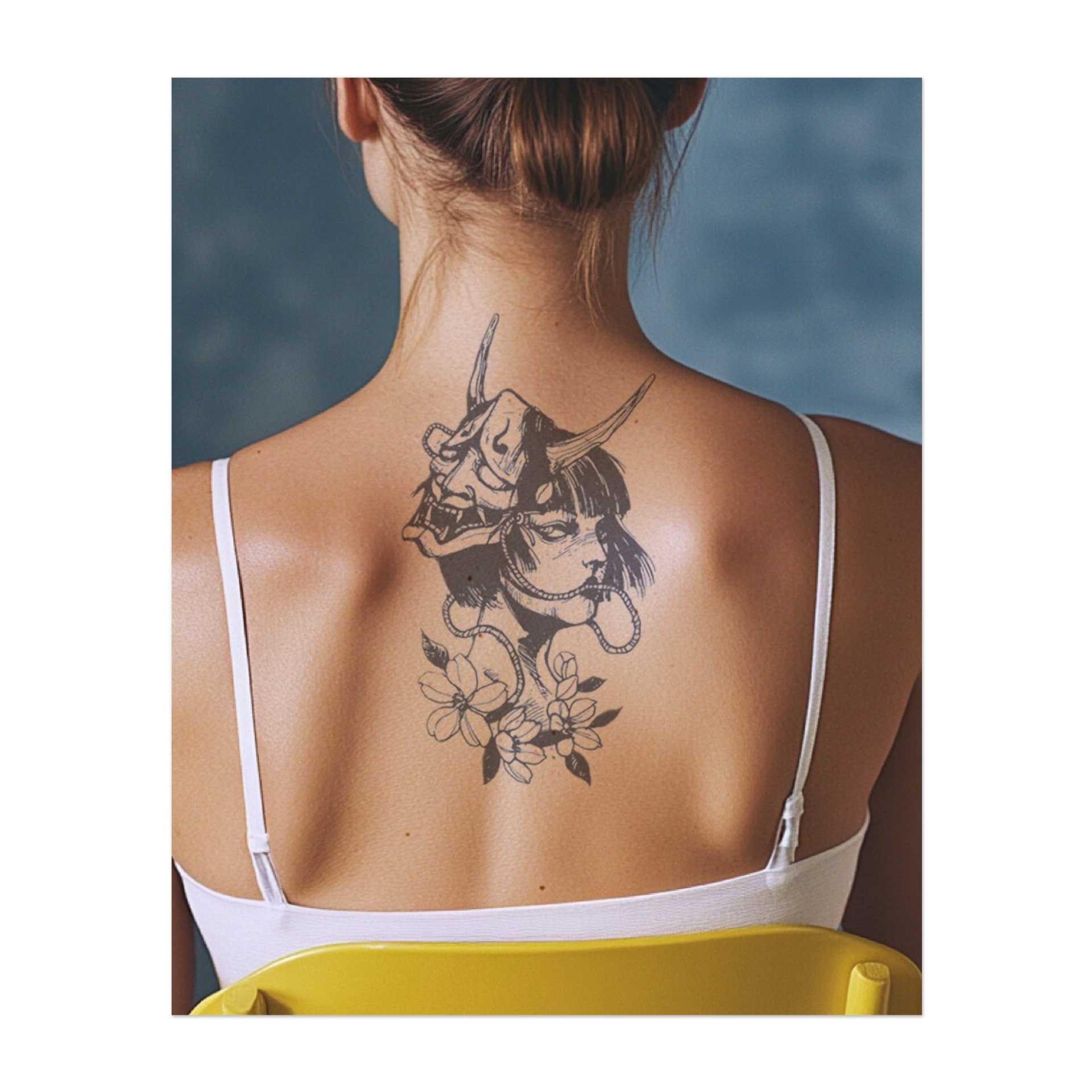 Un tatuaggio sorprendente di una donna che indossa una tradizionale maschera Oni, circondata da delicati fiori. Il disegno combina bellezza e oscurità, simboleggiando forza, mistero e trasformazione. Perfetto per chi abbraccia sia il potere che la grazia.