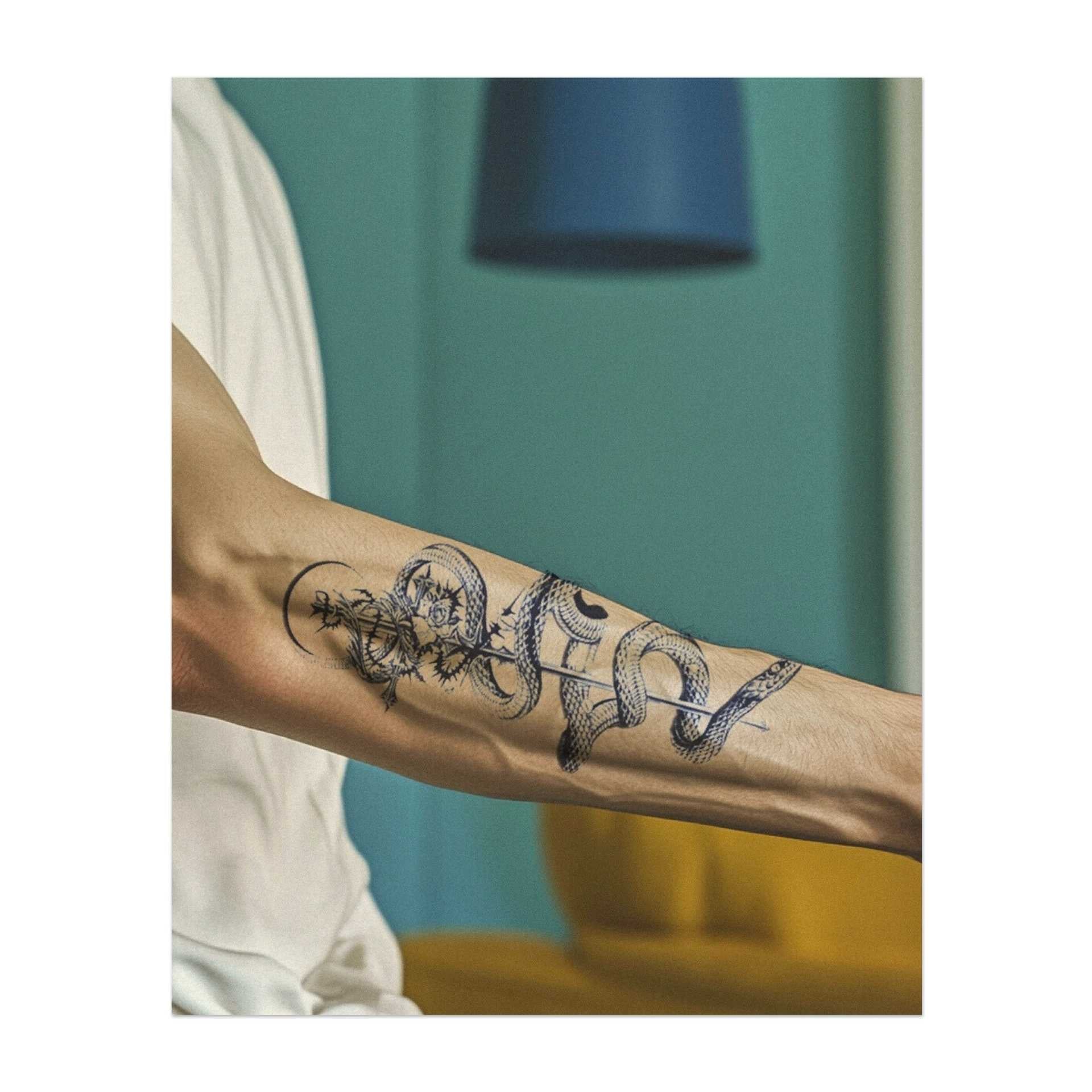 Un grazioso serpente avvolto attorno a un bastone, intrecciato con fiori e coronato in cima. Questo tatuaggio simboleggia guarigione, trasformazione e saggezza, combinando simboli antichi con la bellezza naturale. Perfetto per chi apprezza l'equilibrio e la crescita nel proprio percorso.