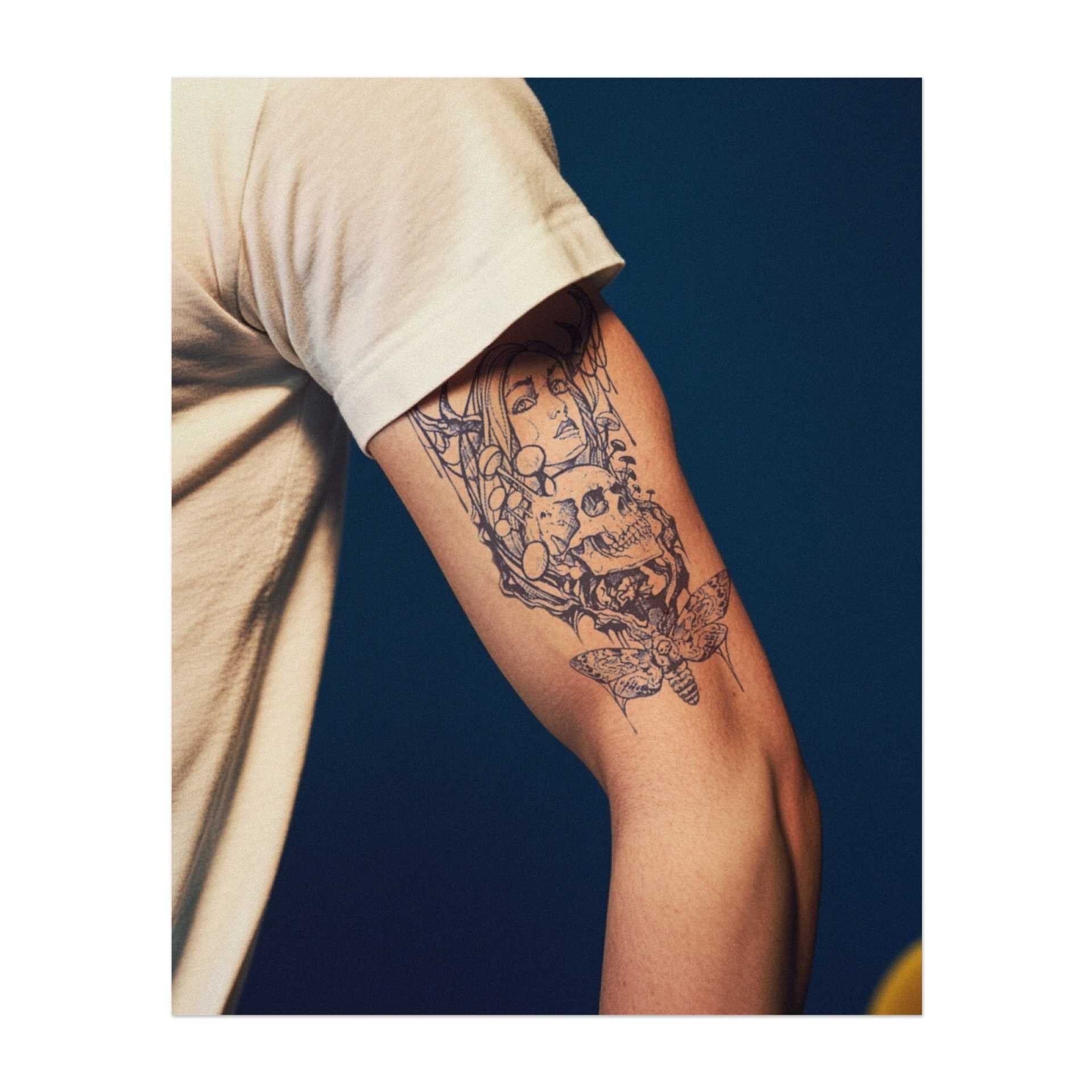 Un tatuaggio mistico raffigurante una donna con corna di cervo, circondata da un teschio, funghi e una farfalla. La luna crescente in alto aggiunge un tocco di magia e mistero. Questo disegno simboleggia la trasformazione, l'equilibrio tra vita e morte e la bellezza dei cicli naturali.