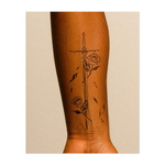 Un tatuaggio minimalista con una linea nera raffigurante una spada ornata intrecciata con rose in fiore e petali cadenti, a simboleggiare bellezza e forza in equilibrio.