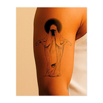 Una figura misteriosa e senza volto si erge, avvolta in una tunica fluente, con le braccia tese sotto un alone oscuro. Questo tatuaggio inquietante evoca anonimato, divinità e ignoto, combinando meraviglia e inquietante serenità in una silhouette minimalista e spettrale.