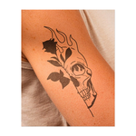 Questo sorprendente tatuaggio bisecato abbina una delicata rosa a un teschio fiammeggiante, simboleggiando la dualità tra vita e morte, bellezza e distruzione. Le sue linee pulite e il netto contrasto esprimono con forza trasformazione e transitorietà.