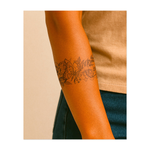 Un grazioso tatuaggio a forma di nastro con fiori che sbocciano e una farfalla circondata da foglie e bacche. Questo tatuaggio simboleggia la trasformazione, la bellezza e il delicato equilibrio della natura.