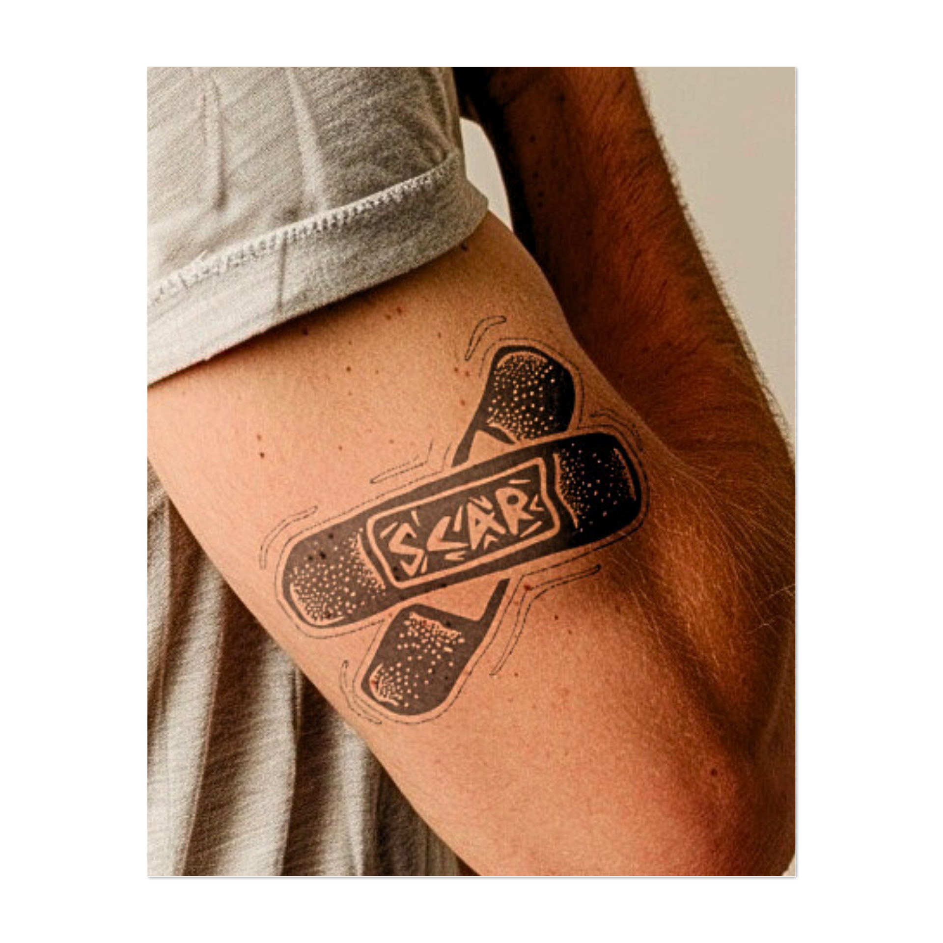 Due bende sovrapposte formano una "X" con la parola "SCAR" chiaramente visibile al centro. Questo tatuaggio temporaneo giocoso ma espressivo combina ombreggiature da fumetto con un audace messaggio di guarigione e forza attraverso l'imperfezione.