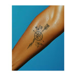 Una bussola decorata con delicati fiori e una piuma simboleggia l'orientamento, l'avventura e la bellezza della natura. Rappresenta un viaggio attraverso la vita, guidato sia dalla direzione che dalla saggezza della natura.