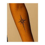 Questo tatuaggio minimalista raffigura una stella luminosa a otto punte con un preciso motivo a punti. Questo disegno simboleggia direzione, speranza e luce interiore, evocando la navigazione celeste e fungendo da simbolo senza tempo di guida attraverso i sentieri più oscuri della vita.