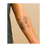 Due serpenti intrecciati, ognuno con un teschio sulla testa, simboleggiano il pericolo, la morte e la rinascita. I serpenti avvolti l'uno attorno all'altro rappresentano l'equilibrio tra vita e morte in un design audace e sorprendente.