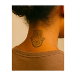 Un tatuaggio minimalista raffigurante una luna crescente con un viso gentile che piange una lacrima. Soffici nuvole turbinano attorno al tatuaggio, conferendogli un'atmosfera sognante e mistica che evoca emozioni e tranquillità attraverso linee delicate.