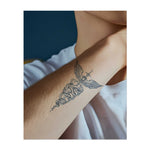 Un tatuaggio minimalista a forma di caduceo, con un bastone alato e due serpenti avvolti attorno ad esso. Questo simbolo rappresenta guarigione, medicina ed equilibrio ed è disegnato con linee chiare e dettagliate.