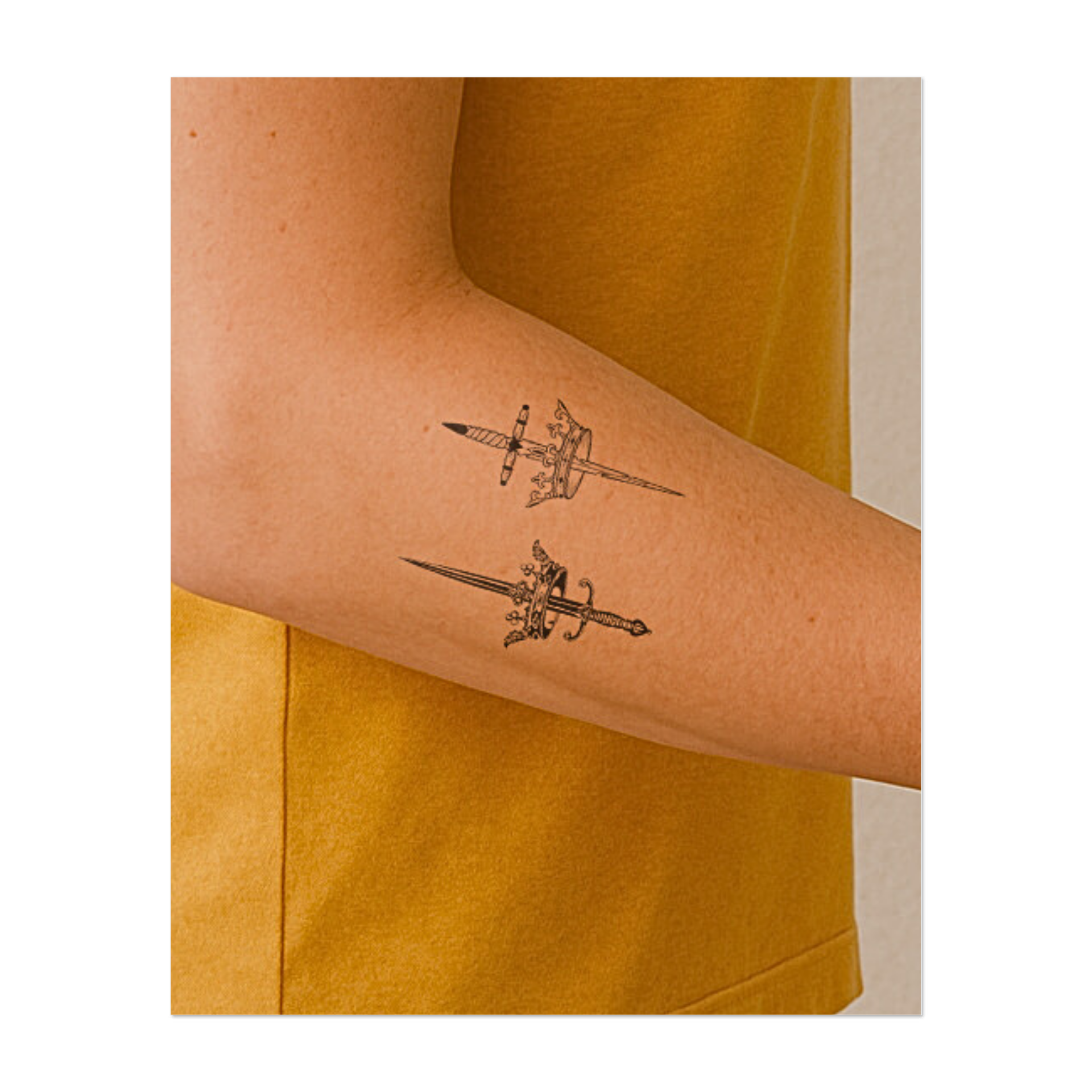 Due spade dettagliate trafiggono le corone reali, simboleggiando potere, sacrificio e sovranità. Questo tatuaggio temporaneo a specchio combina eleganza e precisione medievali, perfetto per una dichiarazione audace ed elegante.