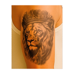 Questo tatuaggio reale raffigura un maestoso leone incoronato con un ornato copricapo reale. Il suo sguardo intenso e la fluente criniera in delicate tonalità di grigio evocano potere, saggezza e nobiltà, simboleggiando leadership, orgoglio e forza incrollabile.