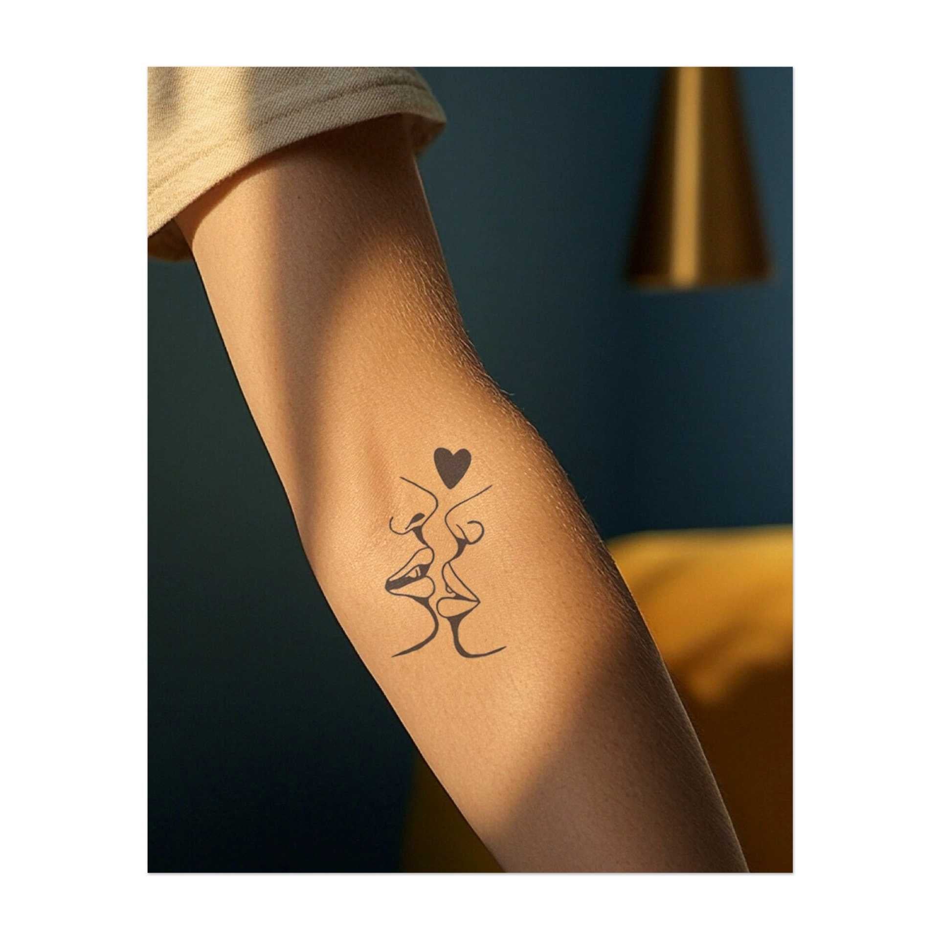 Due volti si uniscono per baciarsi, formando un cuore sopra di loro. Questo tatuaggio rappresenta amore, connessione e intimità, perfetto per chi apprezza i legami emotivi profondi.