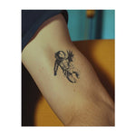 Un astronauta che fluttua nello spazio, con indosso una tuta integrale e le braccia tese. Questo tatuaggio rappresenta la scoperta, l'avventura e il perseguimento dei sogni, perfetto per chi è attratto dall'ignoto e dalle infinite possibilità dell'universo.