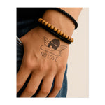 Una maschera con ali d'angelo poggiata sulla scritta "NO LOVE" simboleggia il conflitto tra vulnerabilità e protezione del proprio cuore.