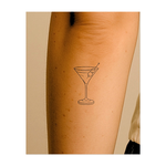 Un elegante disegno a tratteggio di un classico bicchiere da martini, decorato con due olive su uno stuzzicadenti. Questo design raffinato trasuda eleganza e festa, perfetto come simbolo giocoso e sofisticato di vita notturna e svago.